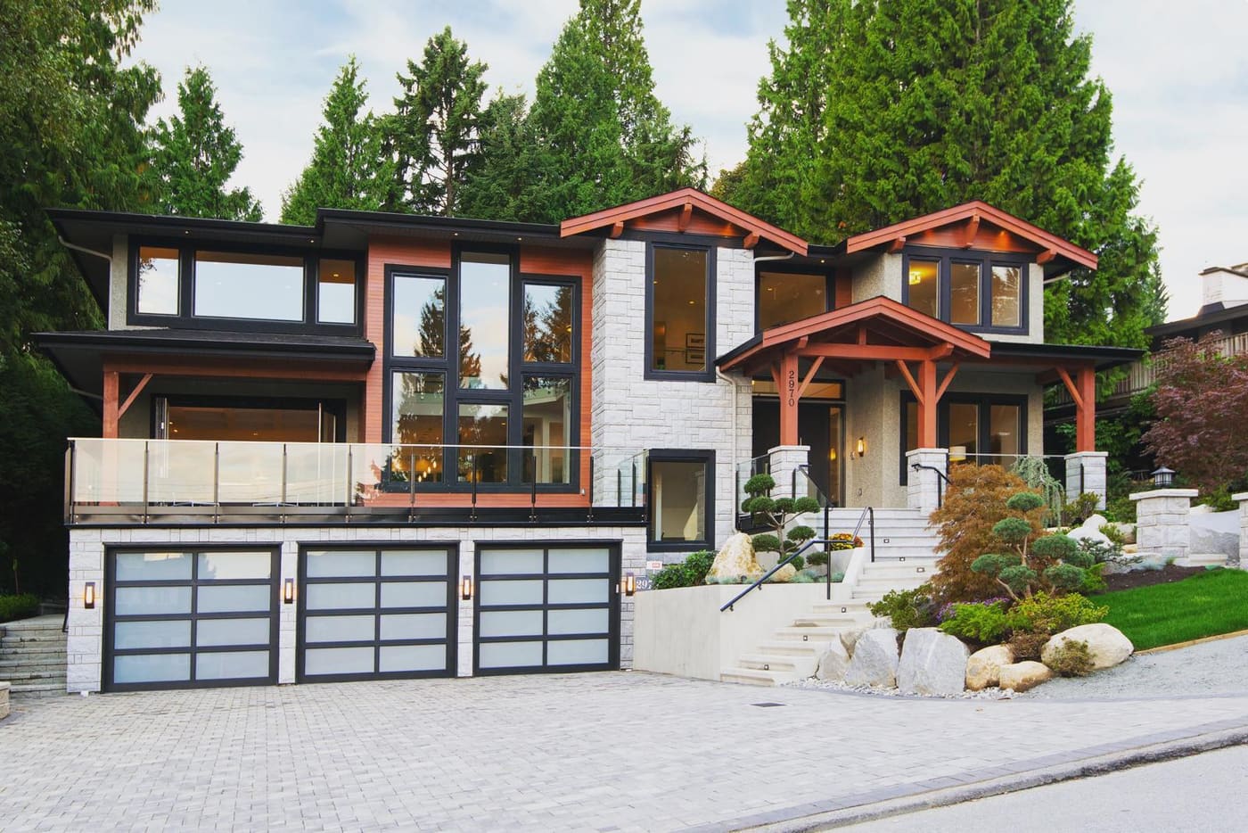 West coast modern home with timber beams, glass garage doors, and a stone retaining wall
